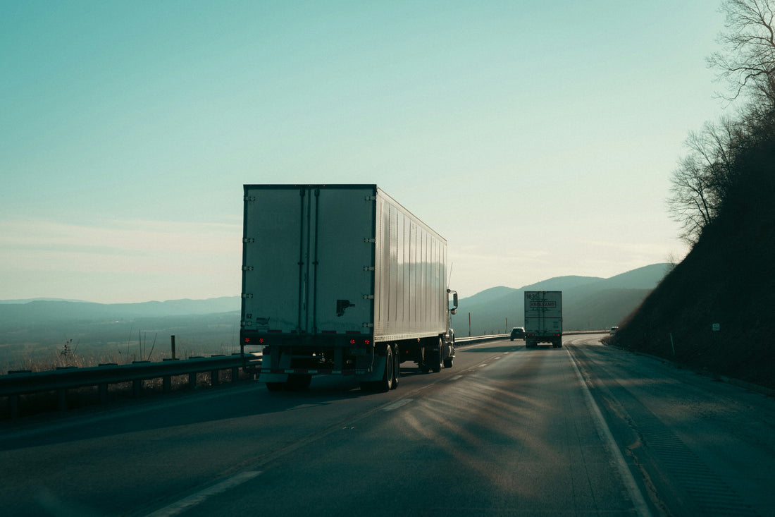 Two semi-trucks driving down a divided highway, the kind of cross-border freight haul where a PARS barcode label keeps the load moving through CBSA